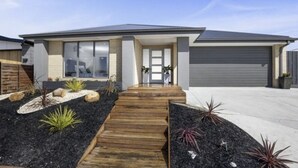 A modern two-story house with a front porch, a garage, and landscaped garden beds.