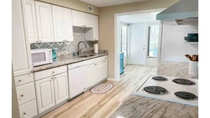 A kitchen with white cabinets, a microwave, a stove, and a patterned backsplash. - Cute Beach House half a block from the beach 🏝 (Ormond Beach)