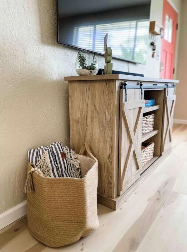 A wooden console table with a television mounted above it, a woven basket with striped fabric, and a red door in the background.
