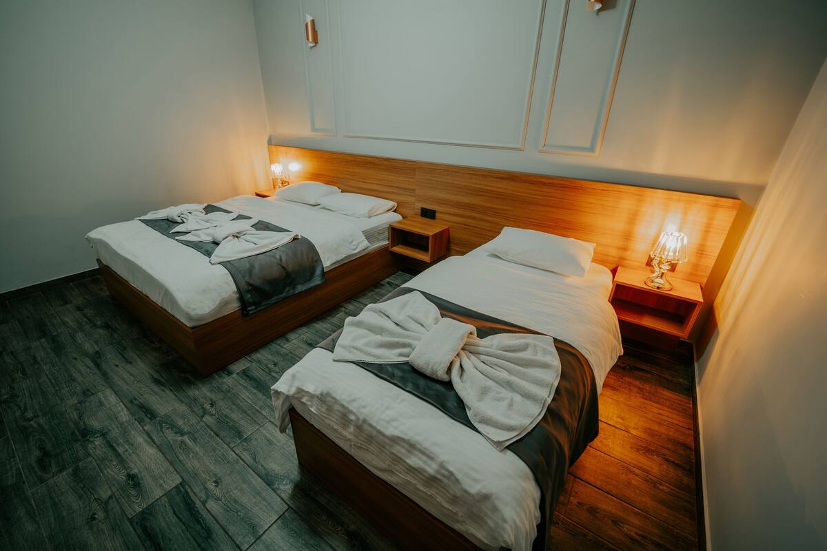 Et hotelværelse med to enkeltsenge, trægavle, sengeborde med lamper og trægulv.