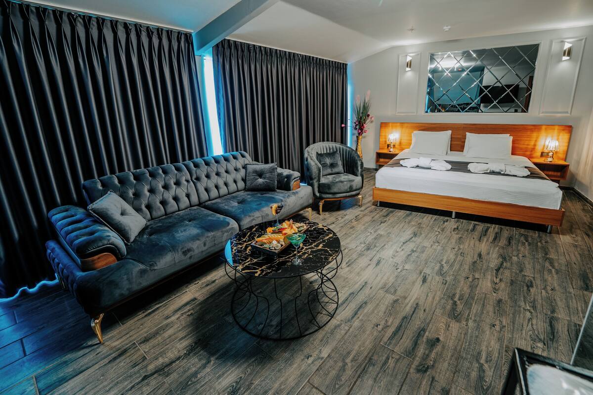 Et moderne hotelværelse med en stor seng, en sofa, et rundt sofabord og et natbord med en lampe.
