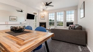 A modern living room with a wooden dining table, blue chairs, a grey sofa, and a fireplace. - Riverside Twin `A` | Balcony | King Bed | Spacious (Fairmont Hot Springs)