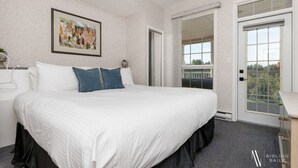 A bedroom with a large bed, a painting on the wall, a window, and a door leading to a balcony. - Riverside Twin `A` | Balcony | King Bed | Spacious (Fairmont Hot Springs)