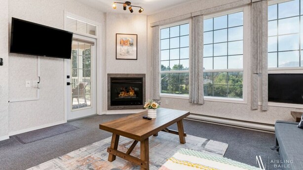 A modern living room with a fireplace, large windows, a flat-screen TV, and a wooden coffee table. - Riverside Twin `A` | Balcony | King Bed | Spacious (Fairmont Hot Springs)
