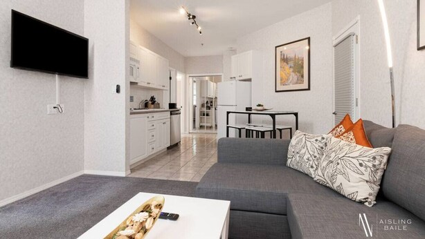 Una sala de estar moderna con un sofá gris, una mesa de centro y un televisor de pantalla plana montado en la pared.