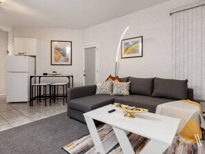 A modern living room with a grey sofa, a white coffee table, and a dining area with a small table and chairs.