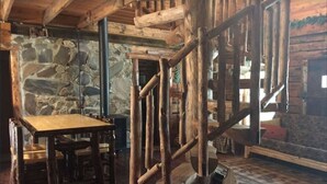 Um interior rústico com parede de pedra, escada de madeira e uma mesa de madeira com cadeiras.