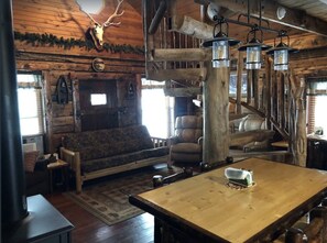 A rustic cabin interior with a wooden dining table, leather sofa, and a staircase. - Cozy Cabin located in the heart of the Black Hills, but close to Deadwood & Lead (Central City)