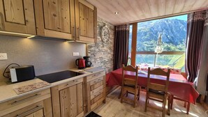 A kitchen with wooden cabinets, a stone backsplash, a red table with chairs, and a view of mountains through a window. - 150m from resort center, 3rd floor, view lake, balcony, tv, ski locker, 40m², Tignes (Tignes)