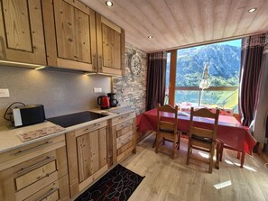 A kitchen with wooden cabinets, a stone backsplash, a red table with chairs, and a view of mountains through a window. - 150m from resort center, 3rd floor, view lake, balcony, tv, ski locker, 40m², Tignes (Tignes)