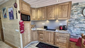 A compact kitchen with wooden cabinets, a stone accent wall, and a red mat on the floor. - 150m from resort center, 3rd floor, view lake, balcony, tv, ski locker, 40m², Tignes (Tignes)