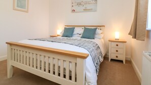 A bedroom with a wooden bed, white bedding, two bedside tables with lamps, a radiator, and a painting on the wall. - 1 Marsh Gardens (Minehead)