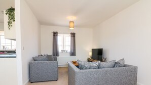 A modern living room with two grey sofas, a flat-screen TV, and a window with curtains. - 1 Marsh Gardens (Minehead)