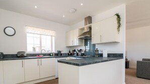 A modern kitchen with white cabinets, a central island, and a window with a view. - 1 Marsh Gardens (Minehead)