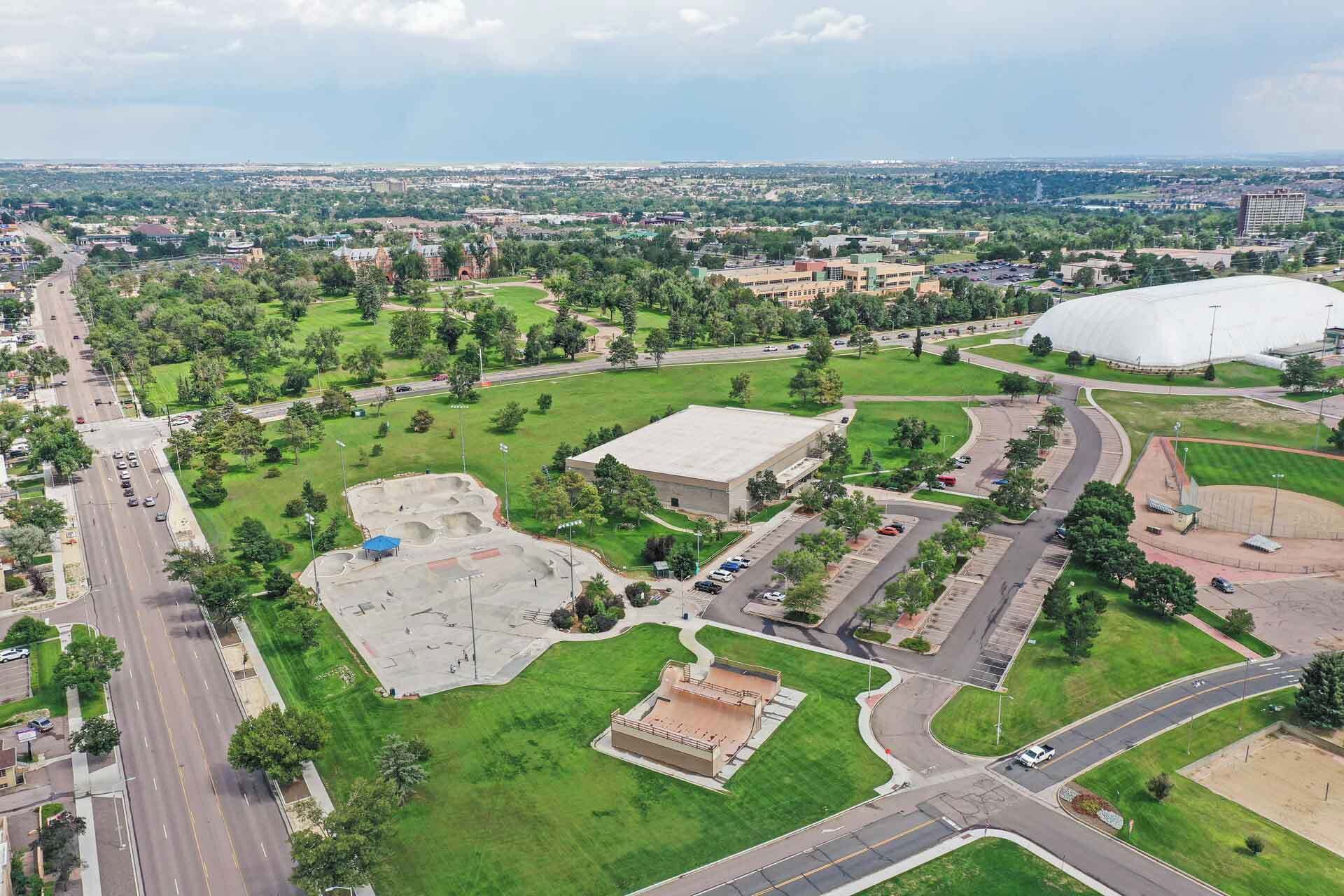 An aerial view of a cityscape with a large stadium, a central building, and surrounding green spaces.