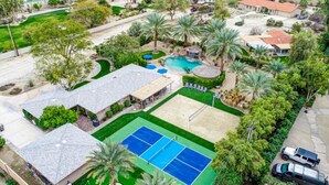 Vue aérienne d’un quartier résidentiel avec un court de tennis, une piscine et plusieurs maisons.