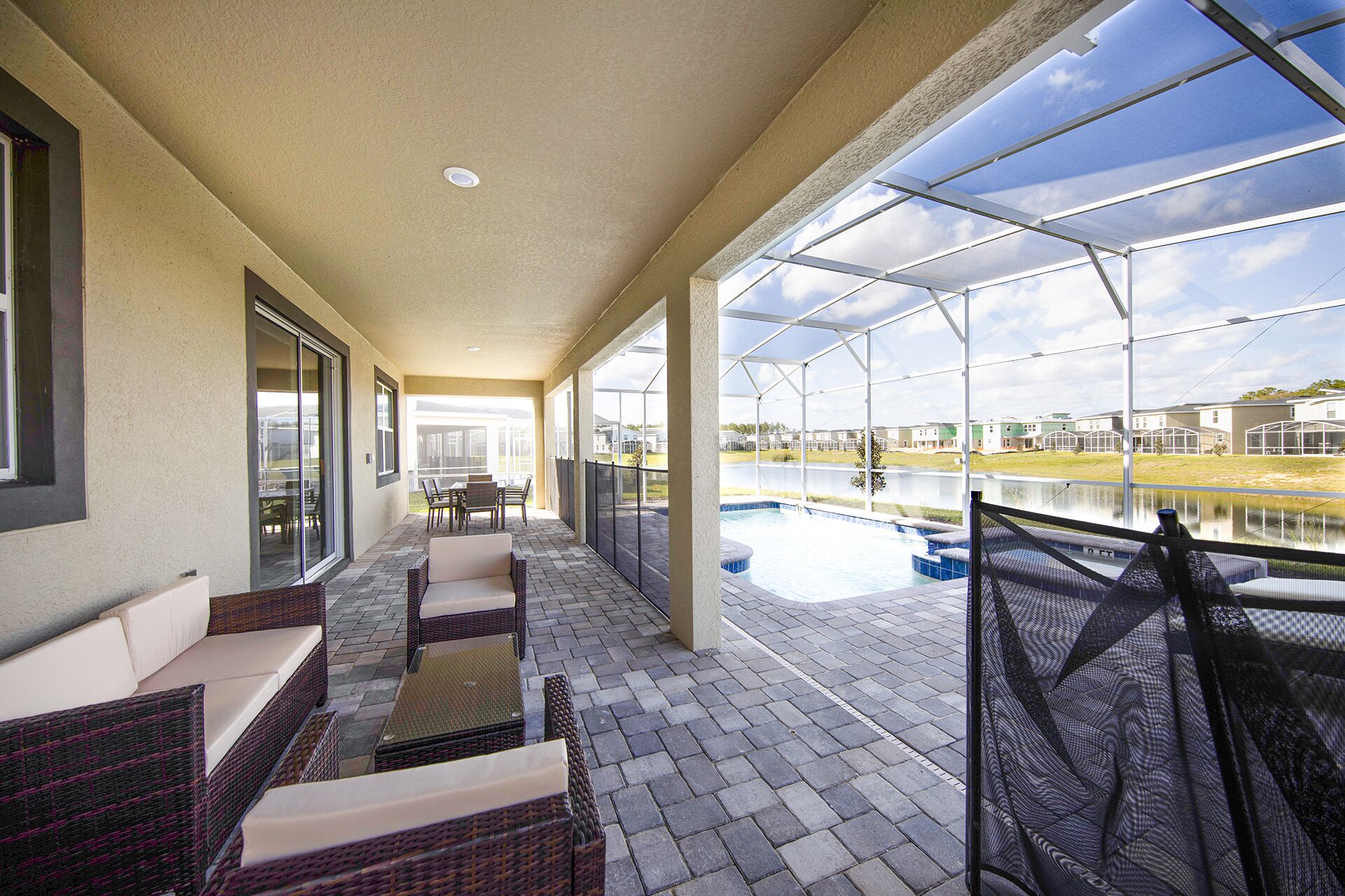 A covered patio with wicker furniture, a pool, and a view of a residential area.