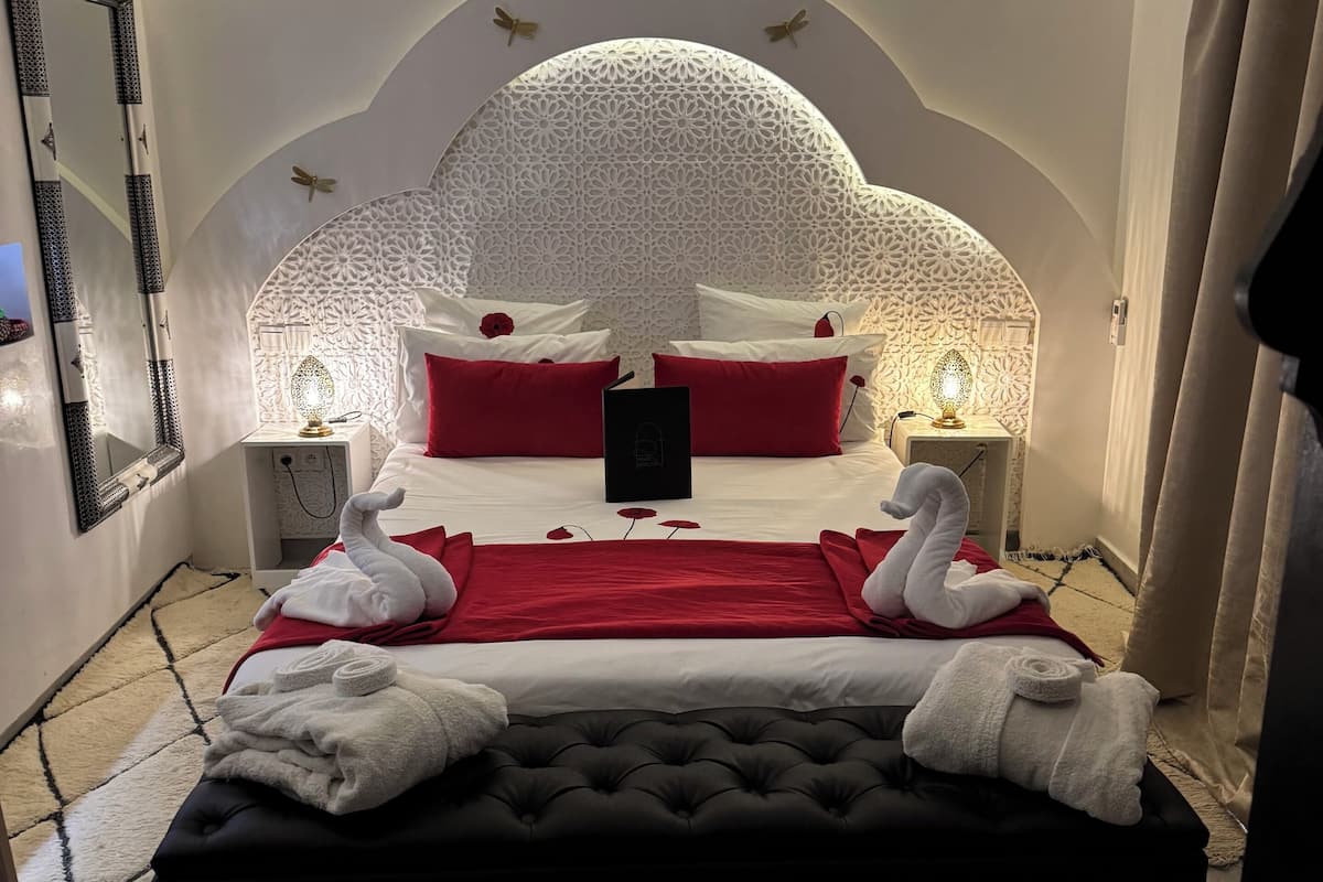 Une chambre à coucher luxueuse, dotée d’un grand lit, d’une tête de lit décorée et d’une petite table ronde sur laquelle est posée une bougie.