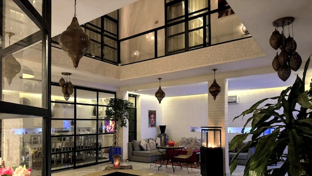 A spacious indoor pool area with a glass enclosure, a seating area with a sofa and table, and decorative hanging lights. - Riad Nolita & Spa Kasbah (Marrakech)