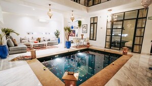 A spacious indoor pool area with a seating area, a dining table, and a large window. - Riad Nolita & Spa Kasbah (Marrakech)