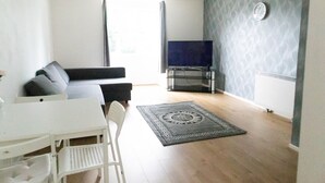 Una sala de estar con un sofá, un televisor, una mesa de comedor con sillas y una alfombra estampada.