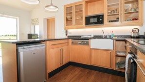 A modern kitchen with wooden cabinets, a built-in microwave, and a dishwasher. - Robins Corner (Weston-super-Mare)