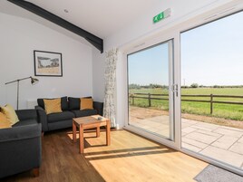 Una sala de estar moderna con un sofá, una mesa de centro y un gran ventanal corredero que da a un espacio exterior con vistas a un campo verde.