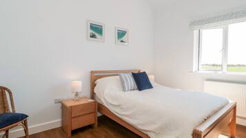 Un dormitorio con una cama de madera, una mesita de noche con lámpara, una silla de mimbre y dos cuadros en la pared.
