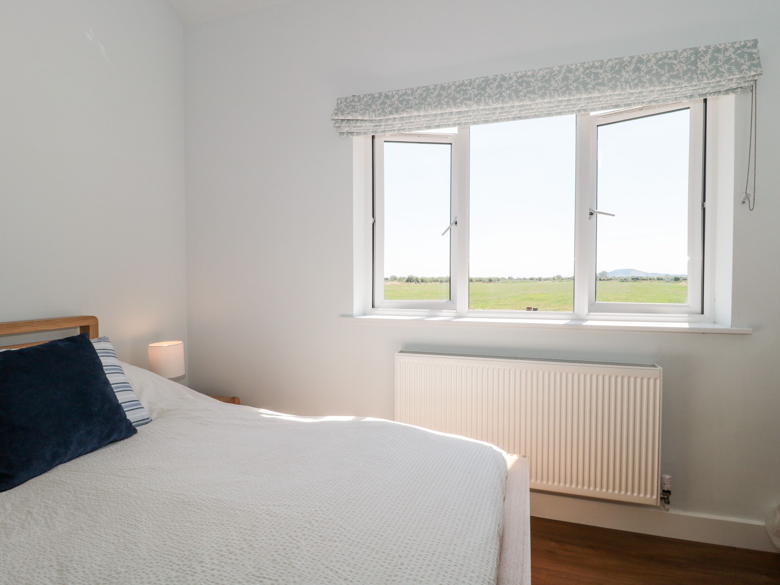 A bedroom with a bed, a window with a view of a field, and a radiator.