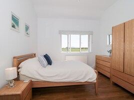 Un dormitorio con cama de madera, una mesita de noche con lámpara, cómoda y ventana con vistas al campo.