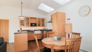 A modern kitchen with wooden cabinets, a central island, and a dining area with wooden chairs. - Robins Corner (Weston-super-Mare)