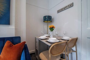 Comedor con una mesa preparada para cuatro, una lámpara y un letrero que dice 'THIS IS OUR HAPPY PLACE'.