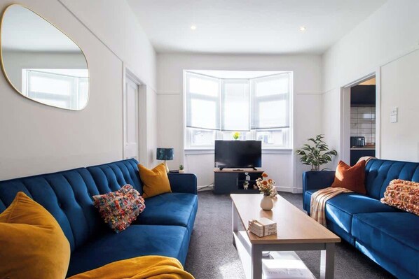Una sala de estar moderna con un sofá azul, una mesa de centro, un televisor y un ventanal grande.