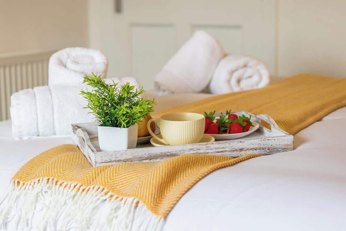 A neatly made bed with a white and yellow striped blanket, a tray with a potted plant, a cup, and a plate of strawberries.