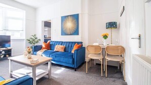A modern living room with a blue sofa, two wicker chairs, a coffee table, and a wall-mounted lamp. - Bella House Fresh 3 Bed Apt in Glasgow  Sleeps 5 (Glasgow City)