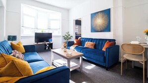 A modern living room with two blue sofas, a coffee table, a TV, and a dining area with a chair and table. - Bella House Fresh 3 Bed Apt in Glasgow  Sleeps 5 (Glasgow City)