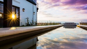 A modern building with a reflective pool, a clear sky, and a sunset. - Fairview House (Keurboomstrand)