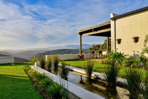A modern building with a covered patio, a small pond with water plants, and a view of distant mountains. - Fairview House (Keurboomstrand)
