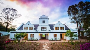A white colonial-style house with a central tower, multiple windows, and a well-maintained garden with pathways. - Fairview House (Keurboomstrand)