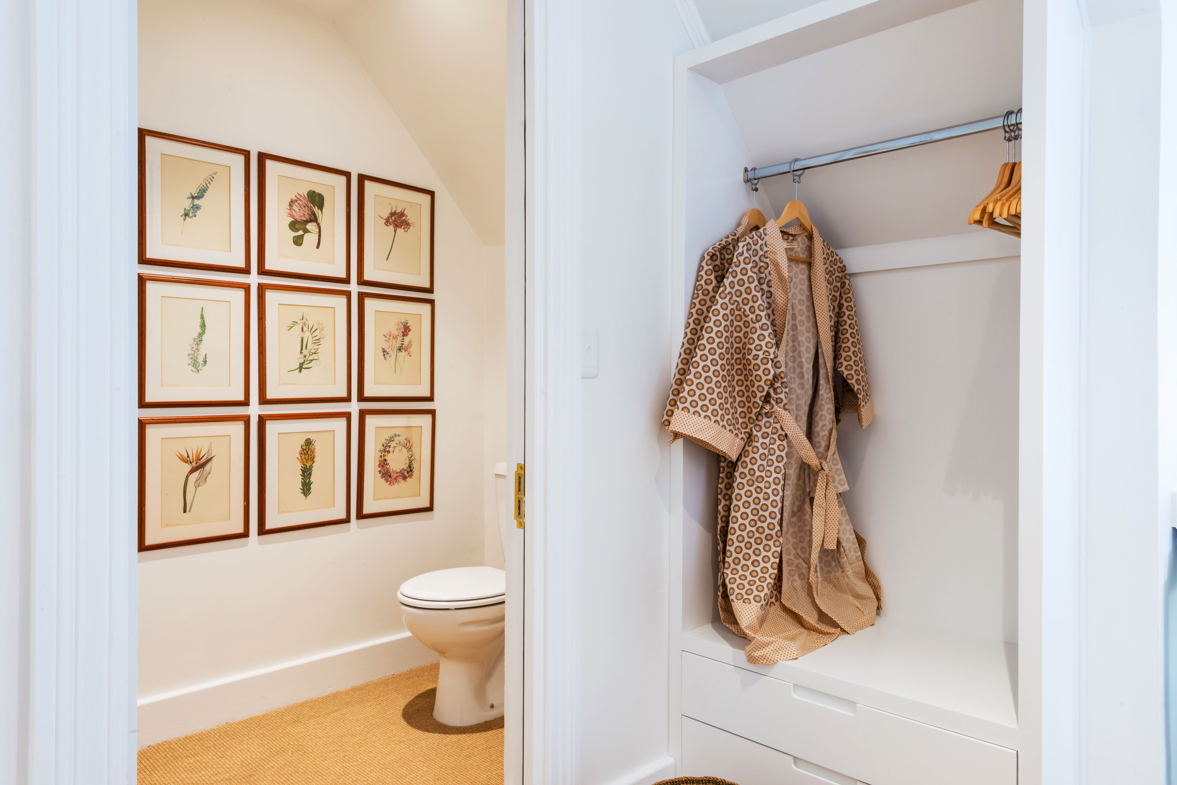 Een badkamer met toilet, douche en een rek met handdoeken. Er hangen omlijste botanische prints aan de muur.