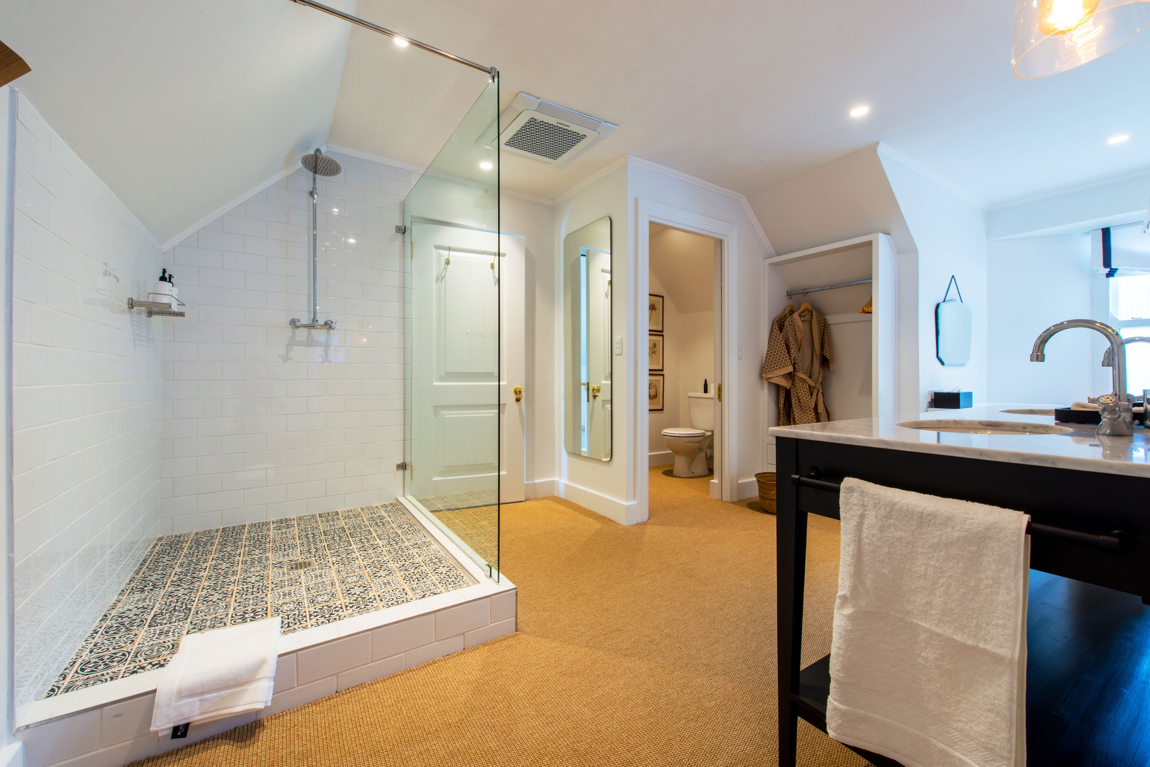 A modern bathroom with a glass-enclosed shower, a bathtub with patterned tiles, and a large mirror above the sink.