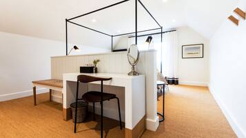 A bedroom with a white desk, a chair, a small plant, a mirror, and a bed with a white headboard.
