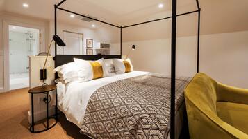 A modern bedroom with a four-poster bed, bedside lamps, and a yellow chair.