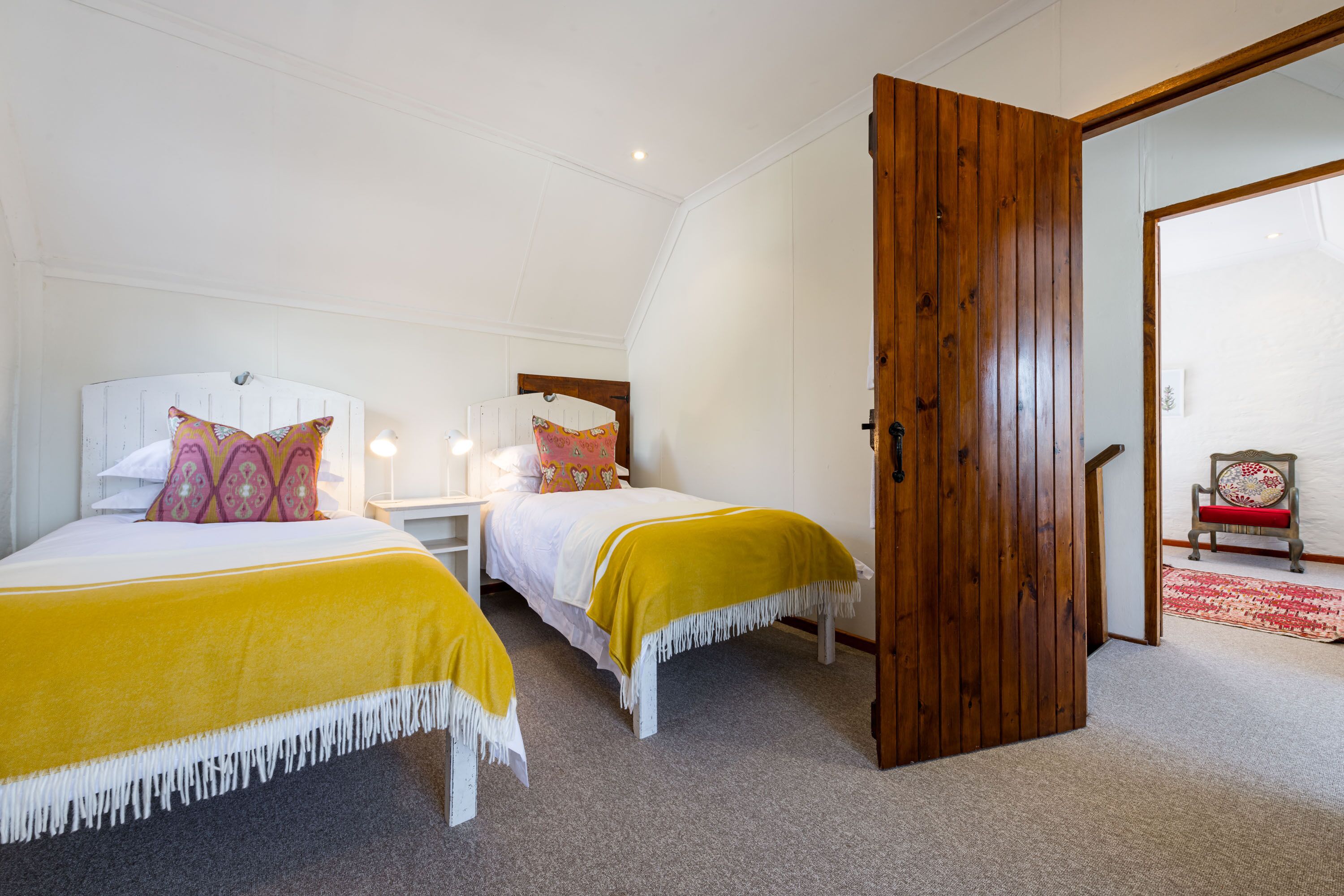 Um quarto com duas camas, uma porta de madeira, uma mesa de cabeceira e uma cadeira.