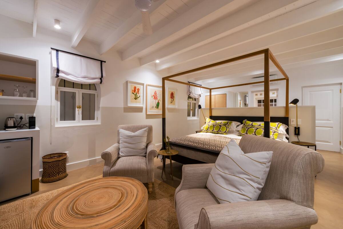 A bedroom with a four-poster bed, a sofa, a chair, a small table, and a bedside lamp.