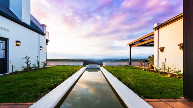 A modern building with a central water feature, surrounded by well-maintained grass and a clear sky. - Fairview House (Keurboomstrand)