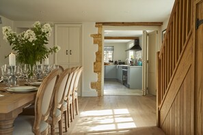 A dining area with a wooden table set for a meal, a vase of flowers, and a view into the kitchen.