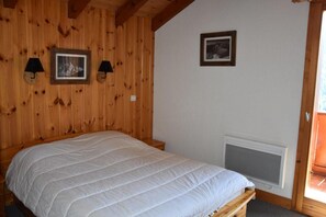 A bedroom with a wooden paneled wall, a bed with a white duvet, two wall-mounted lamps, and a window with a view. - 8th floor, balcony, fireplace or stove, tv, 85m², Champagny-en-Vanoise (Champagny-en-Vanoise)