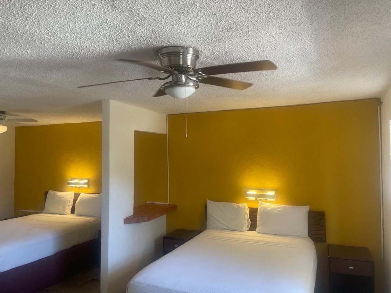 A hotel room with two beds, a ceiling fan, and bedside lamps.