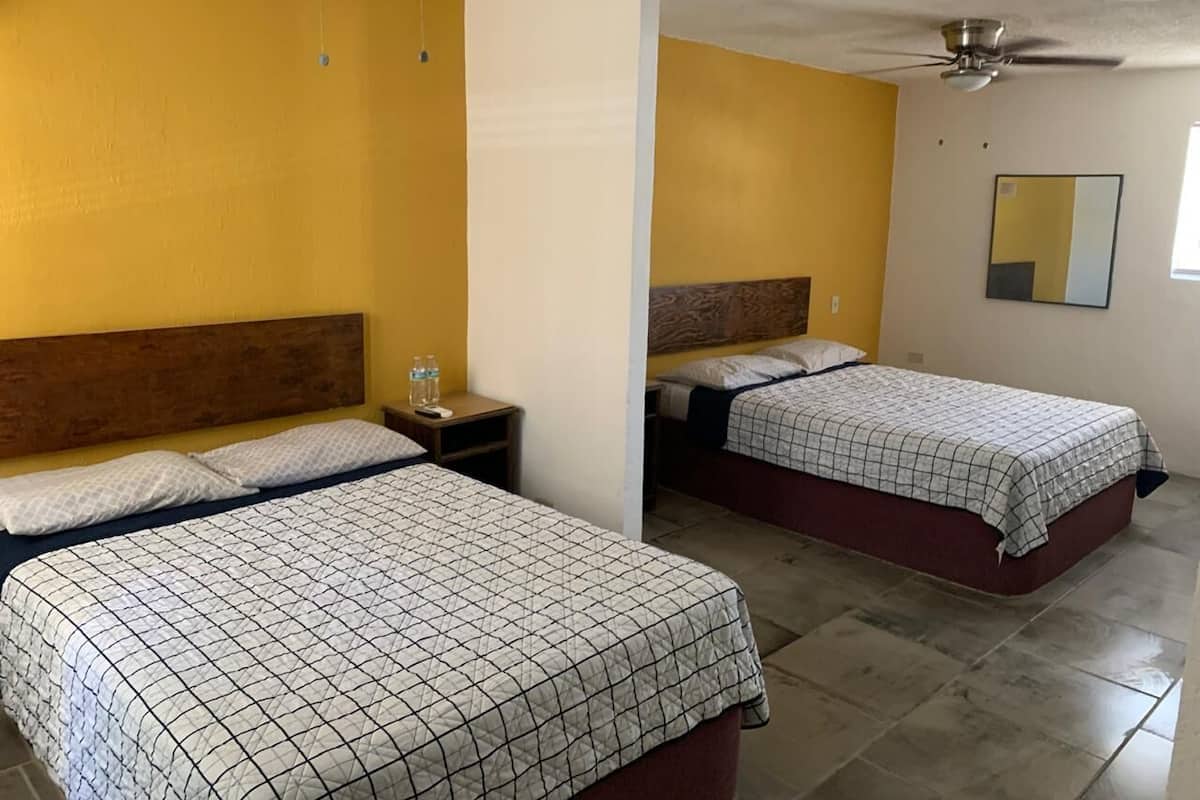A hotel room with two beds, a ceiling fan, and a mirror on the wall.